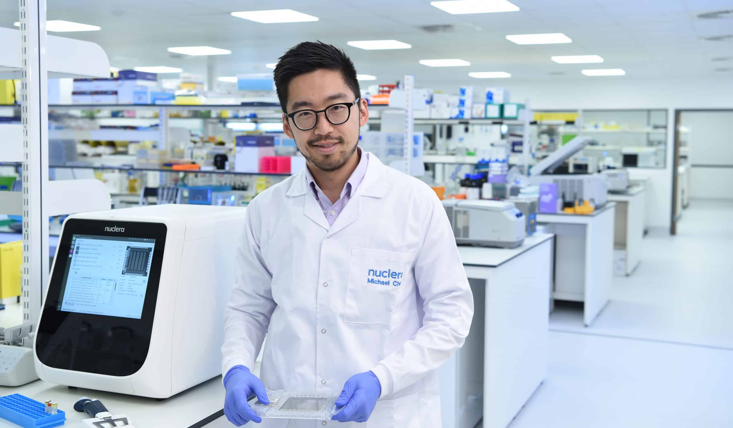 dr Michael Chen standing with eProtein Discovery holding smart cartridge in the lab